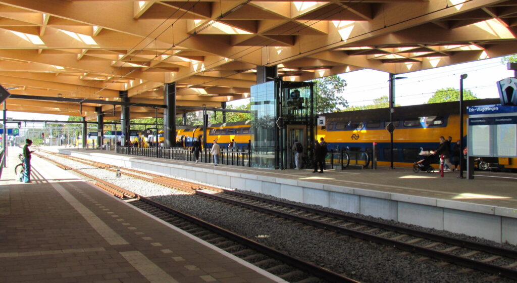 Perron van station Ede-Wageningen onder de houten kap, met een gele intercity langs het perron