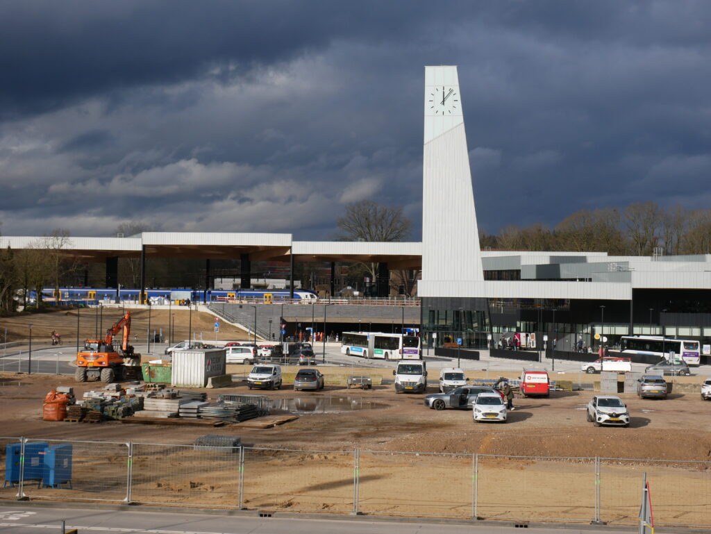 Het nieuwe stationsgebouw van Ede-Wageningen met klokkentoren en houten kap, met bussen op de voorgrond