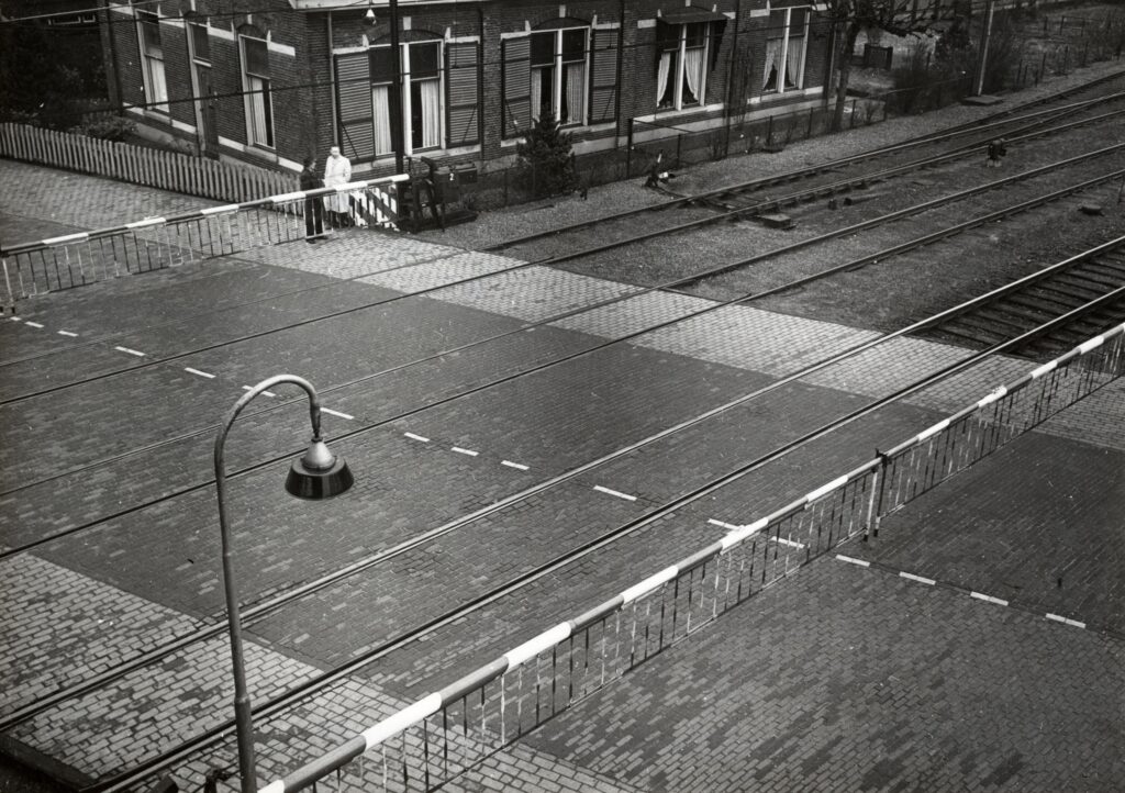 Spoorwegovergang in de Stationsweg-Bennekomseweg bij station Ede-Wageningen in 1954, met gesloten overwegbomen en de voormalige opzichterswoning